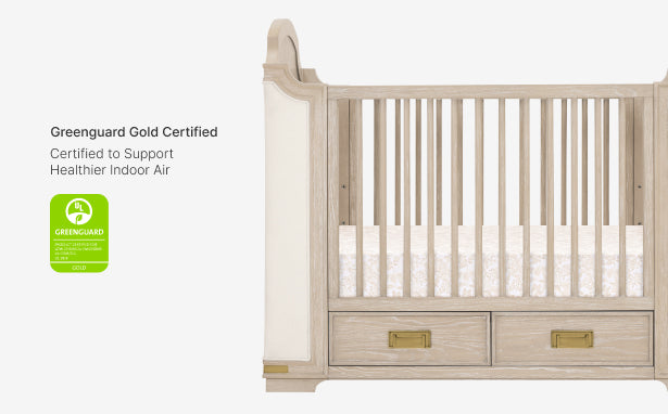 Wooden crib with white mattress and Greenguard Gold certification label on a white background