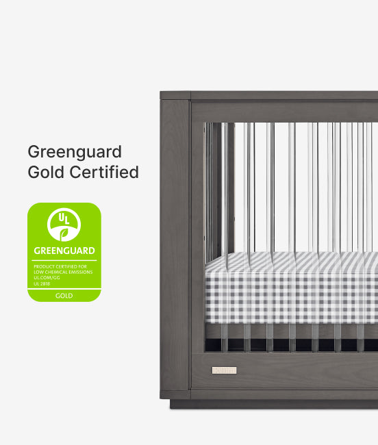 Gray crib with a checkered mattress and Greenguard Gold Certified label on a white background