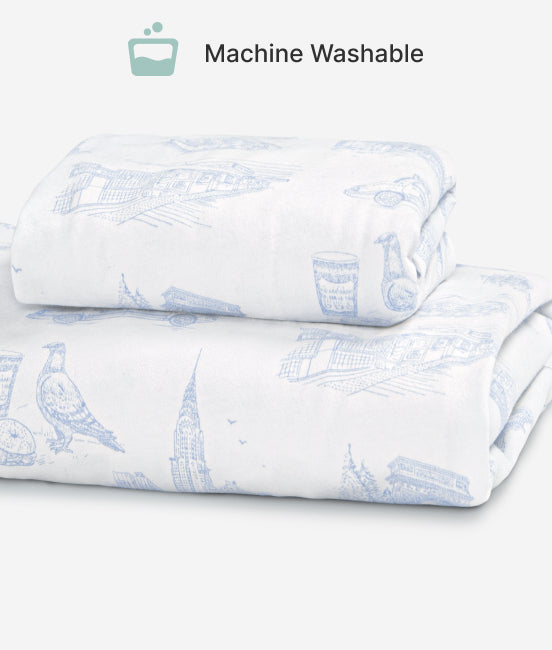 Folded white bed sheets with blue bird pattern on a light gray background, labeled 'Machine Washable'.
