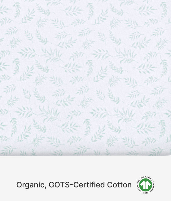 Patterned fabric with small green leaves on a light blue background, featuring GOTS certification logo.