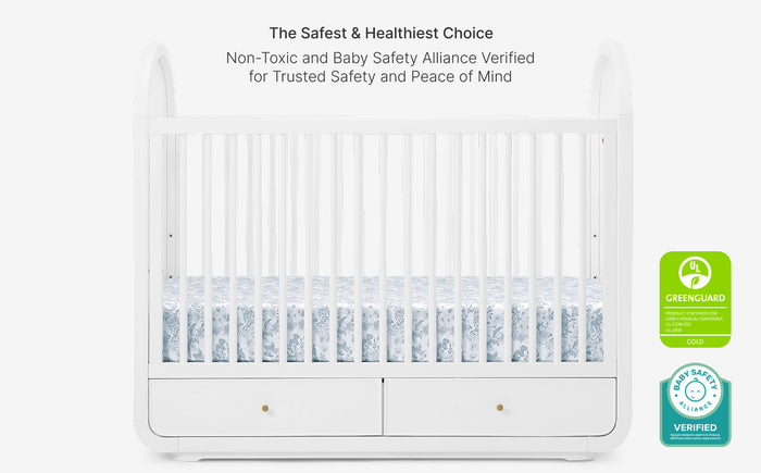 White crib with blue bedding and safety certification logos on a white background