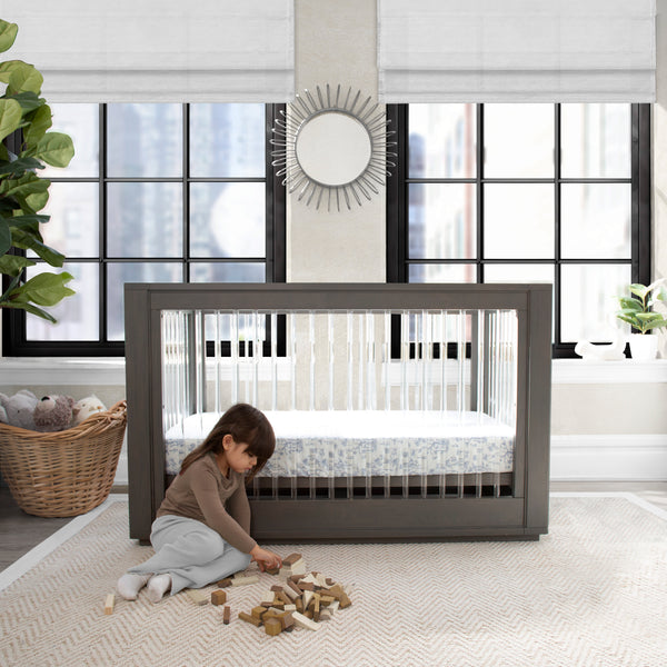 Child playing with toys on the floor next to a crib in a modern room with large windows.