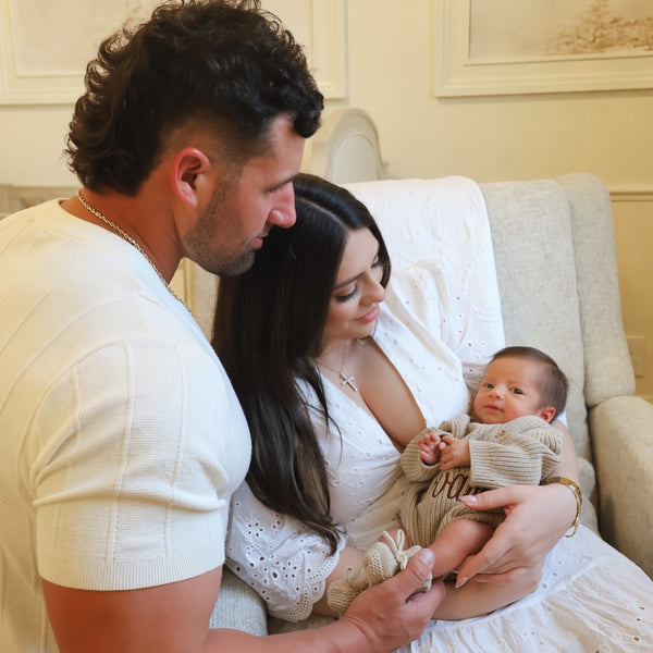 Man and woman holding a baby in a cozy room with decorative wall art.